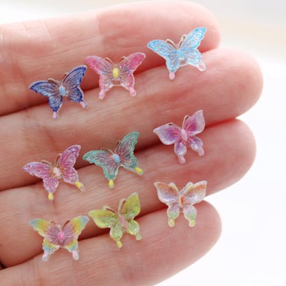 Colorful butterfly-shaped earrings held in a hand against a white background