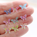 Colorful butterfly-shaped earrings held in a hand against a white background