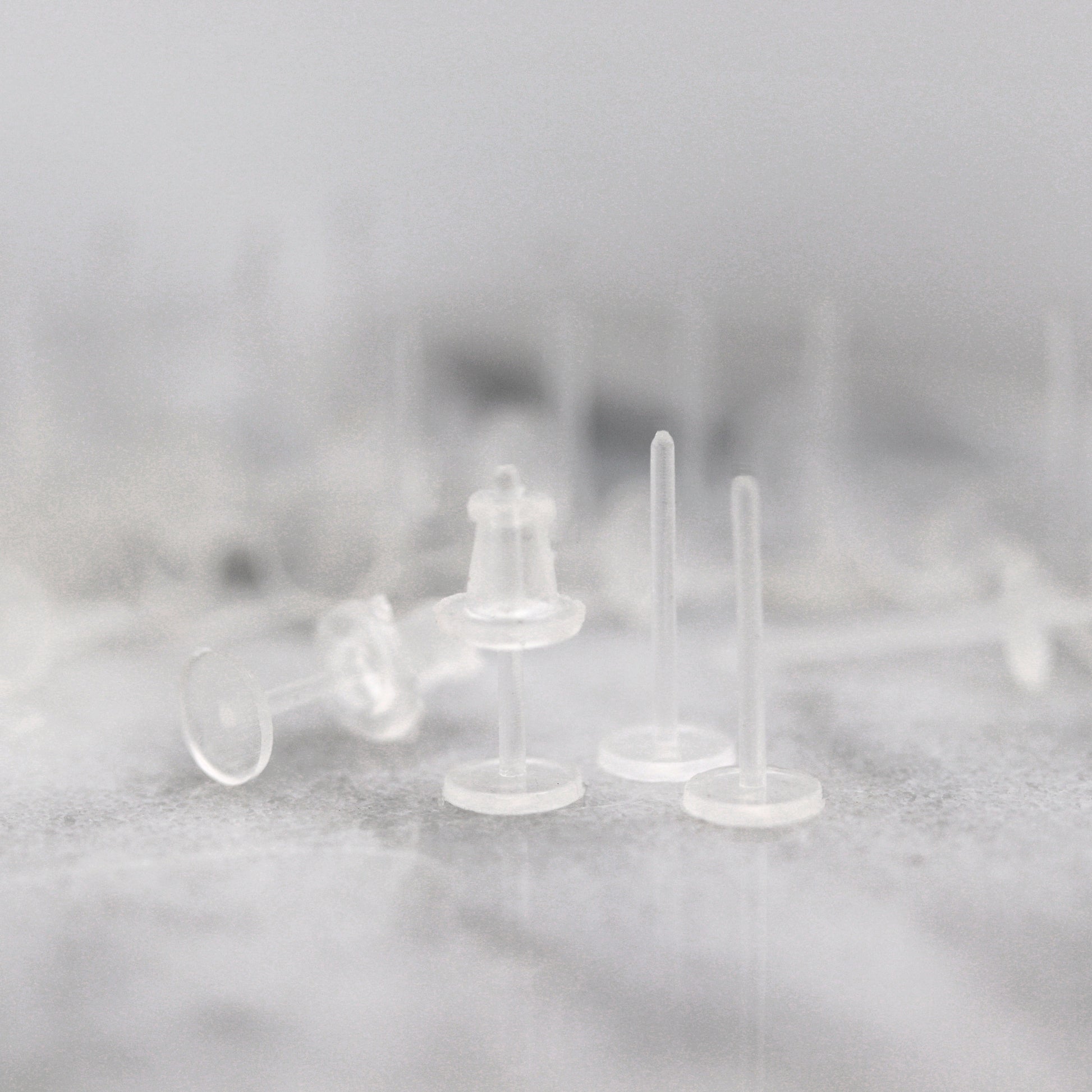 A set of clear plastic earring posts with rubber earring backs placed on a surface.
