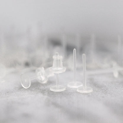 A set of clear plastic earring posts with rubber earring backs placed on a surface.