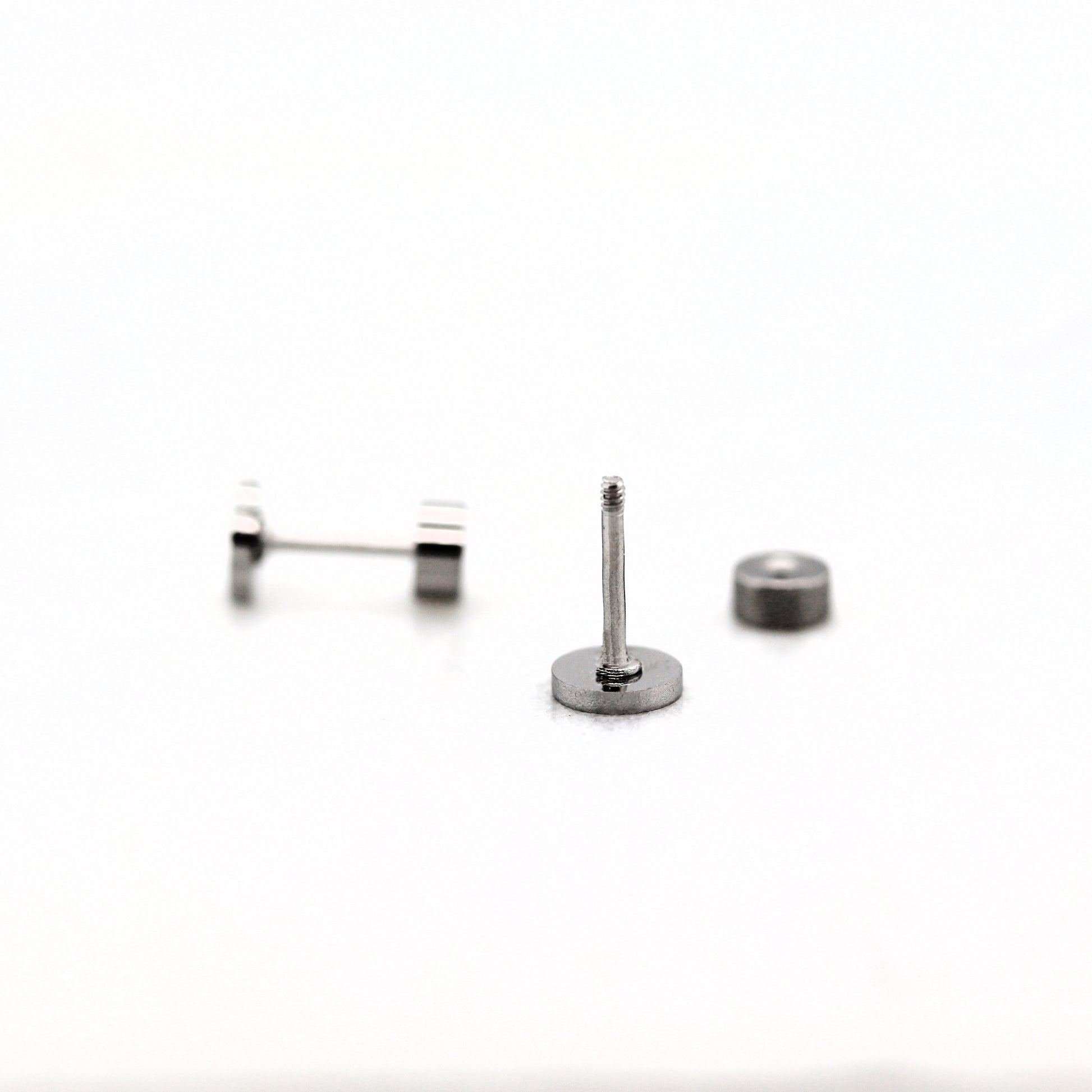 A stainless steel flat screw back earring post with a threaded post, accompanied by two small flat pads for attachment.