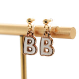 Gold earrings with 'B' charms on a gold stand against a white background