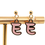Pink 'E' earrings on a gold stand against a white background