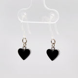 Black heart-shaped earrings on plastic hooks hanging on a clear earring stand.