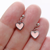 Pink heart-shaped invisible clip on earrings held between fingers on a white background