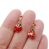 Red ladybug earrings with gold accents held between fingers on a white background