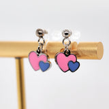 Heart-shaped earrings with pink and blue hearts on a gold stand against a white background
