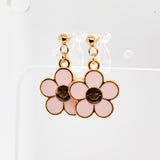 Pink flower-shaped earrings with smiley face centers on a white background