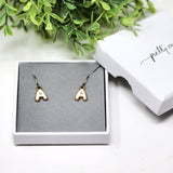 Gold letter 'A' earrings in a white box with greenery in the background