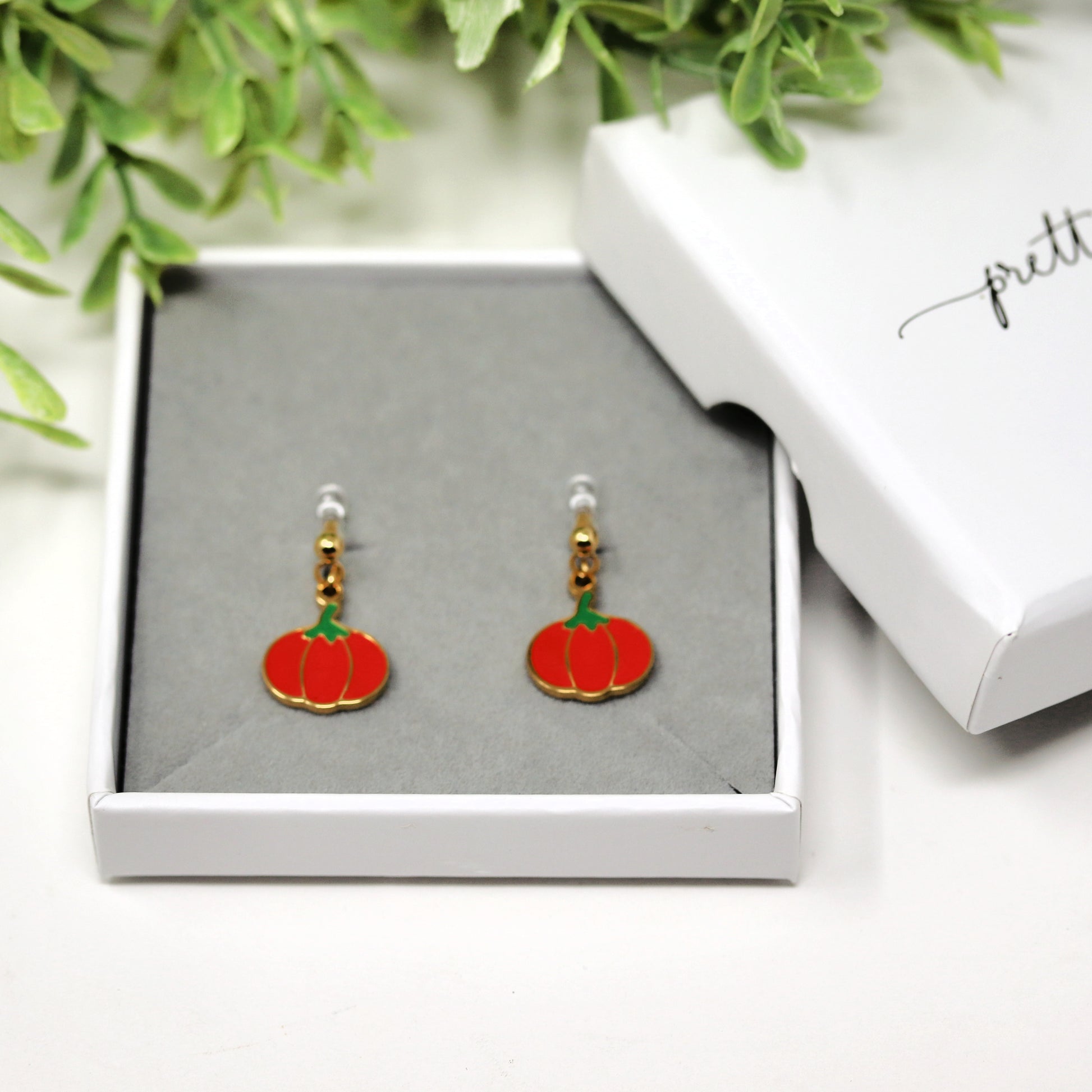 Pumpkin-shaped earrings in a jewelry box with greenery in the background
