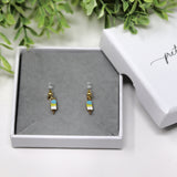 Pair of tiny blue ice cream cone earrings in a white box with a green leafy background