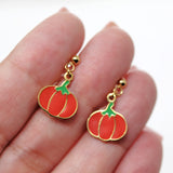 Pumpkin-shaped earrings with gold rims held between fingers on a white background