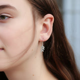 Close-up of an ear wearing silver leaf earrings and a silver stud earring.
