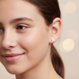 Close-up of an ear with two small earrings: a bunny ear-shaped earring and a clear gemstone.