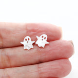 Small ghost-shaped earrings held between fingers on a white background