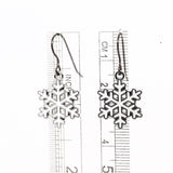 Snowflake earrings with a ruler for scale on a white background