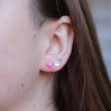 Close-up of an ear with two earrings: a purple heart and a silver rhinestone stud.