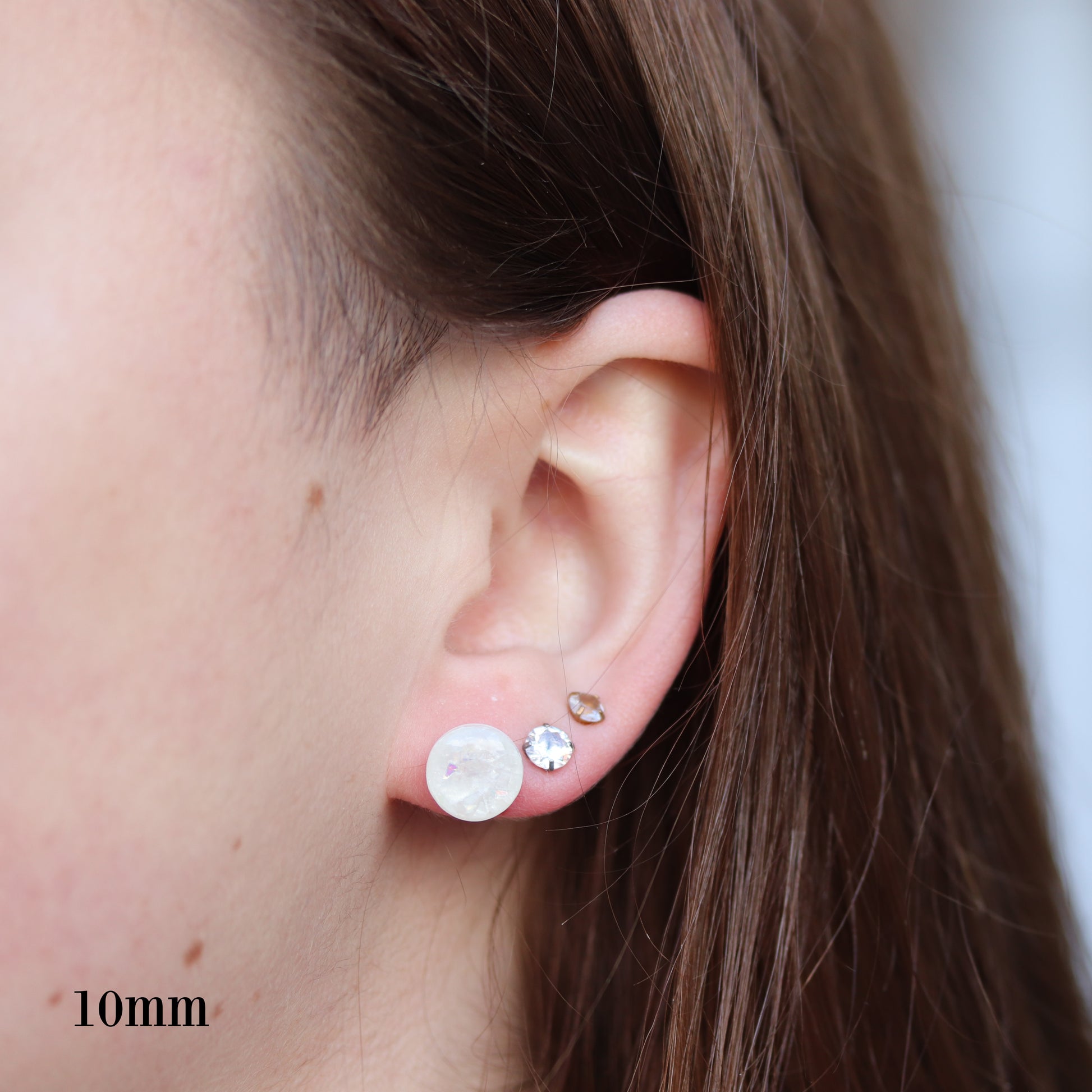 Close-up of an ear wearing two mm white opalescent resin earrings with a blurred background