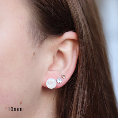 Close-up of an ear wearing two mm white opalescent resin earrings with a blurred background