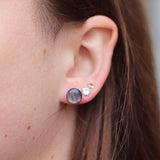 Close-up of an ear wearing black and pourple opalescent earrings with a neutral background