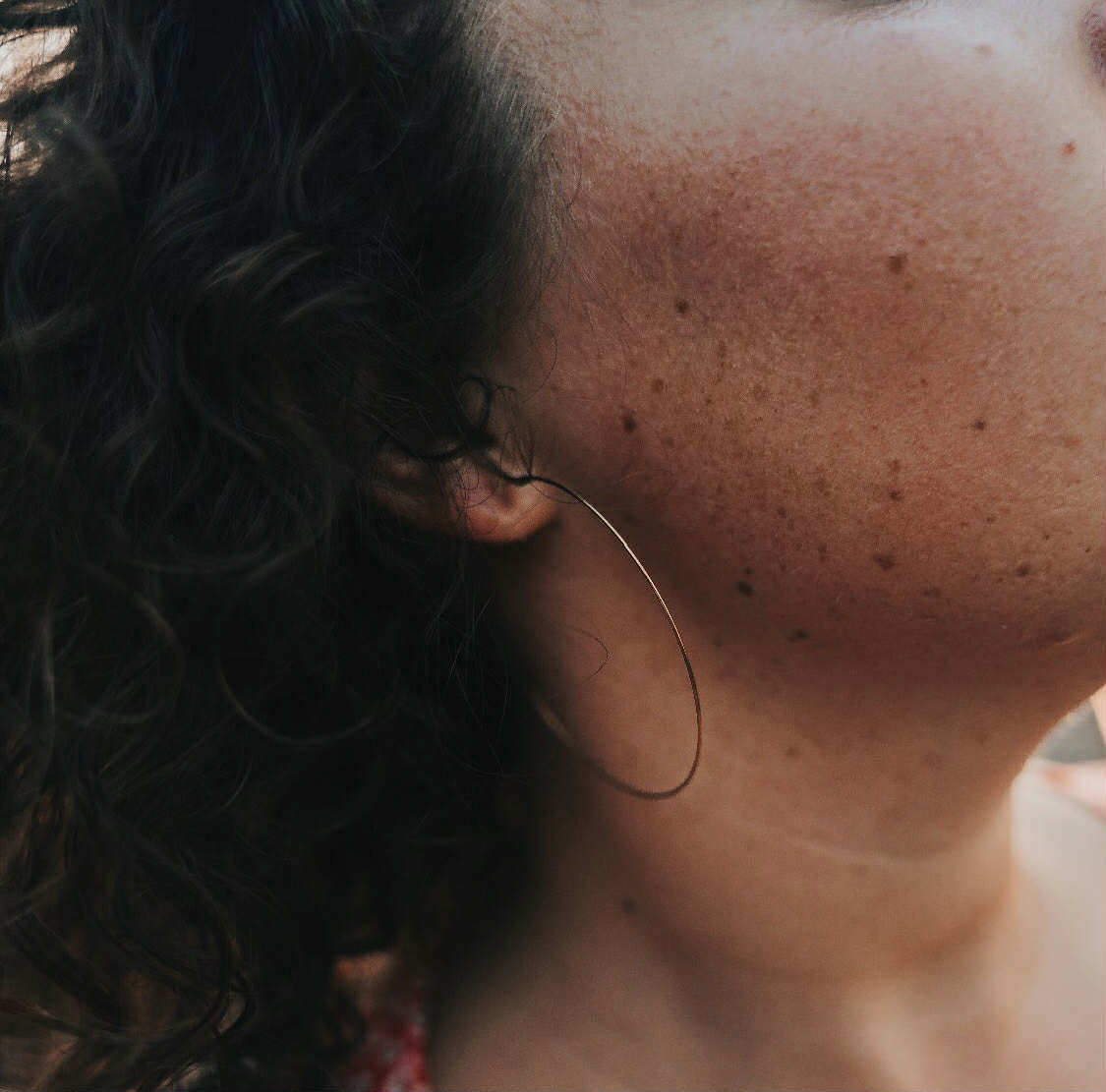 Close-up of an ear with a long hair strand, showing skin texture and freckles wearing wire hoop earrings