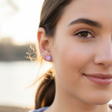 Close-up of an ear with two earrings: a small round earring and a purple flower-shaped earring.