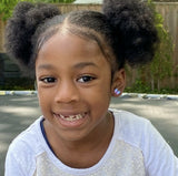 Young girl with pigtails smiling outdoors with purple/blue butterfly stud earrings