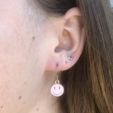Close-up of an ear with a pink smiley face earring.