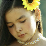 Close-up of a person with a yellow flower in their hair, a yellow flower earrings and a floral necklace.