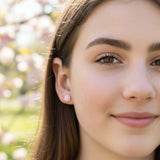 Close-up of an ear wearing a pink flower-shaped earring with a blurred background