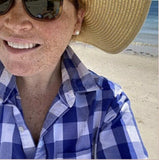 Person wearing a straw hat and blue checkered shirt on a beach with 10mm pearl earrings