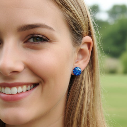 model wearing A pair of blue  glitter filled resin earrings with round cabochons.