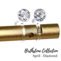 A pair of clear cubic zirconia stud earrings mounted on a gold-colored post, part of the Birthstone Collection for April.