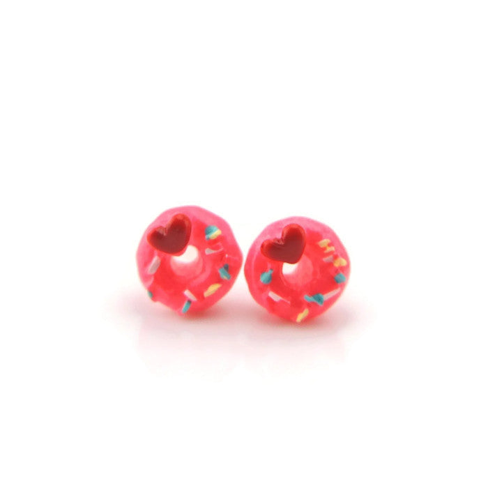 A pair of pink donut-shaped stud earrings with multicolored sprinkles and a red heart pattern on top, displayed against a white background.
