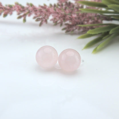 A pair of rose quartz stone earrings with a plastic post design, displayed on a white surface with pink floral accents in the background.
