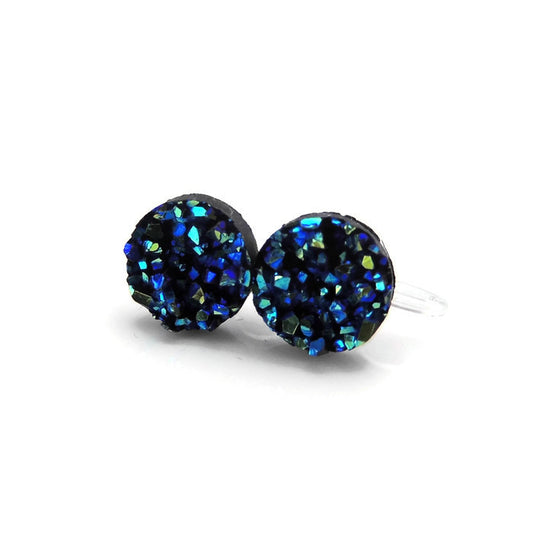 A pair of faux druzy stud earrings with a blue and black pattern, featuring resin material and visible through a clear post system.