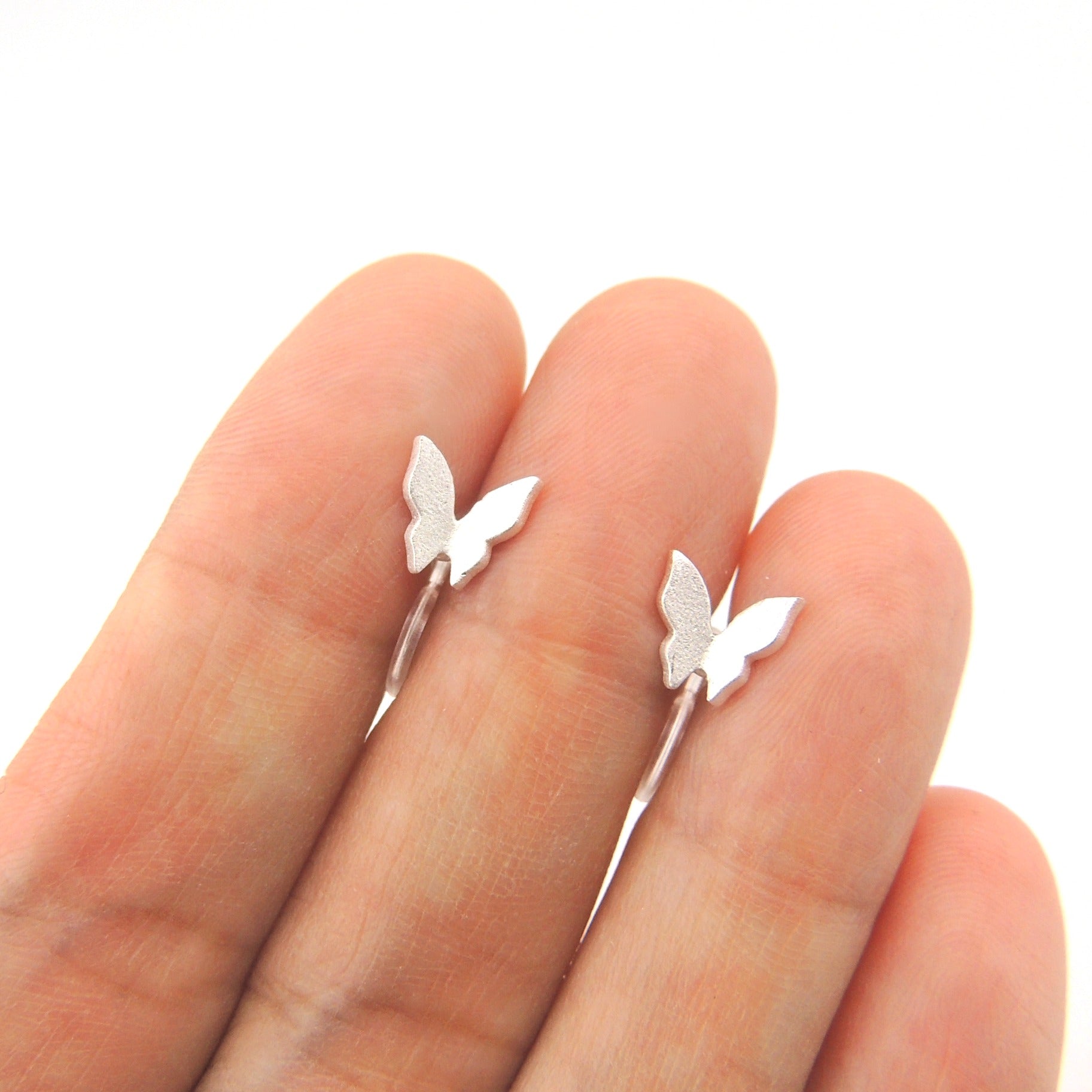 A pair of silver-tone butterfly stud earrings displayed on a person's hand, showing the size and design of the earrings.