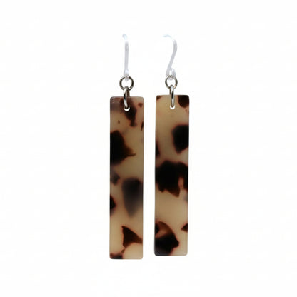A pair of tortoise shell grey acrylic bar dangle earrings displayed on a white surface.