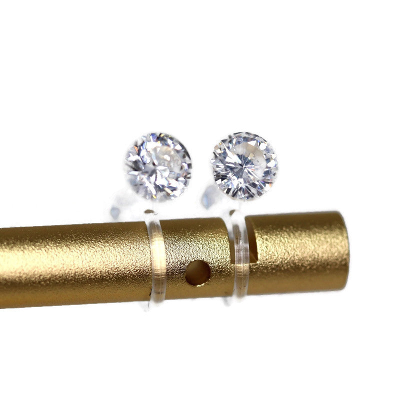 A pair of clear cubic zirconia stud earrings attached to a gold-colored surface with a white clear post system for clip-on earrings.