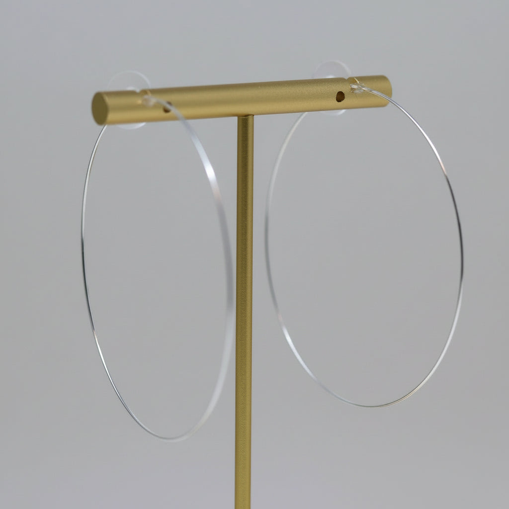 Thin wire hoop earrings with a gold-tone plastic post, displayed on a white stand, with flowers in the background.