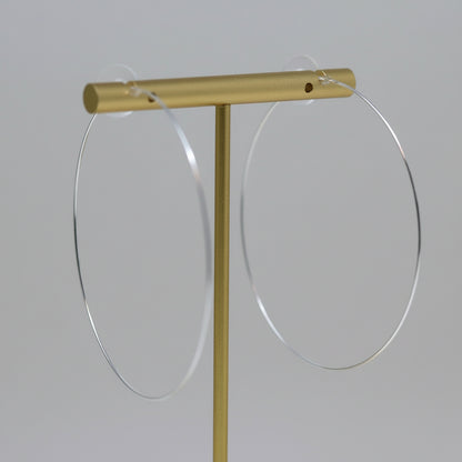 Thin wire hoop earrings with a gold-tone plastic post, displayed on a white stand, with flowers in the background.