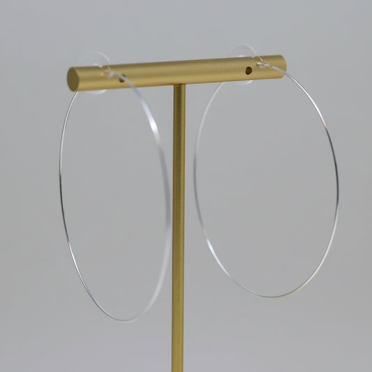 Thin wire hoop earrings with a gold-tone plastic post, displayed on a white stand, with flowers in the background.