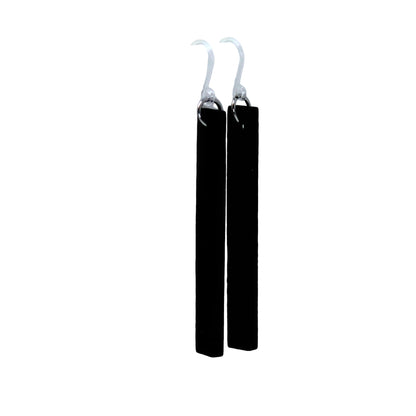 A pair of black wooden dangle earrings with a plastic hook, displayed hanging from the edge of a white cup, with a blurred flower in the background.