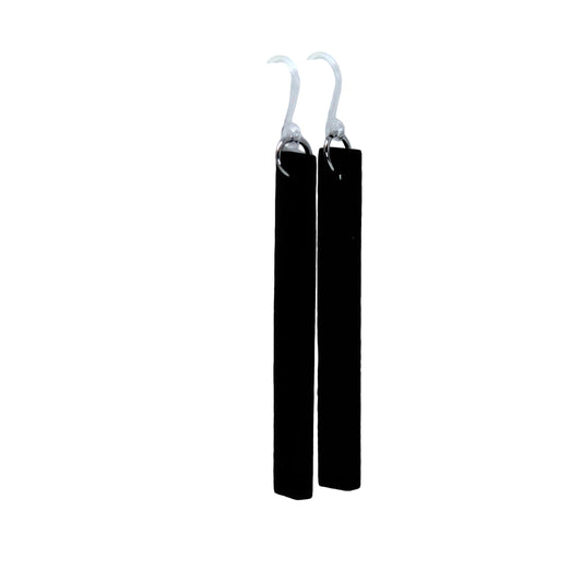 A pair of black wooden dangle earrings with a plastic hook, displayed hanging from the edge of a white cup, with a blurred flower in the background.