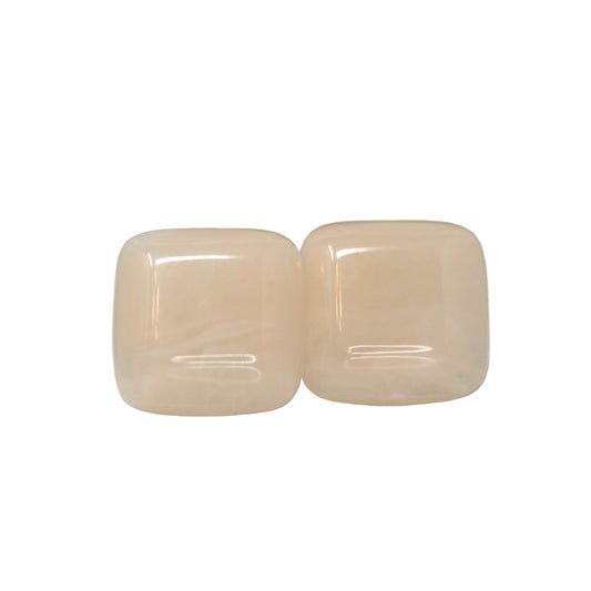 A pair of large square cabochon stud earrings in a flesh-like color, displayed against a reflective white background.