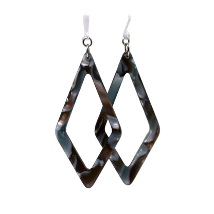 A pair of acrylic dangle earrings with a rhomboid pattern in blue and green shades, displayed on a white surface with a floral background.