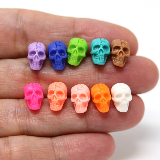 A selection of skull-shaped stud earrings in various colors displayed on a person's hand.