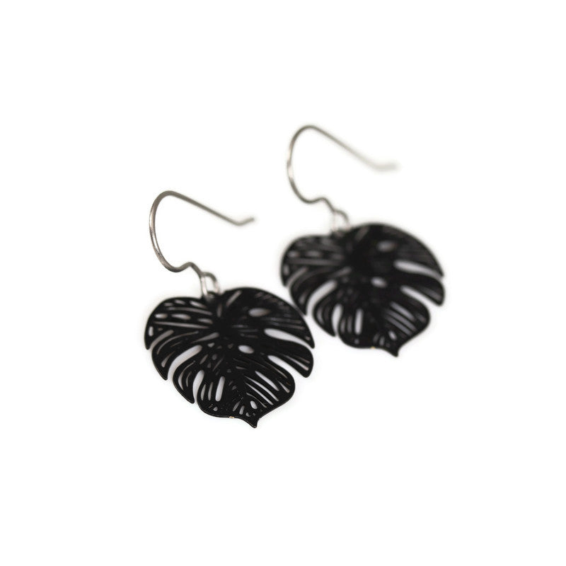A pair of black metal dangle earrings cut in the shape of a Monstera leaf.