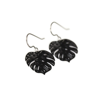 A pair of black metal dangle earrings cut in the shape of a Monstera leaf.