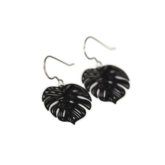 A pair of black metal dangle earrings cut in the shape of a Monstera leaf.